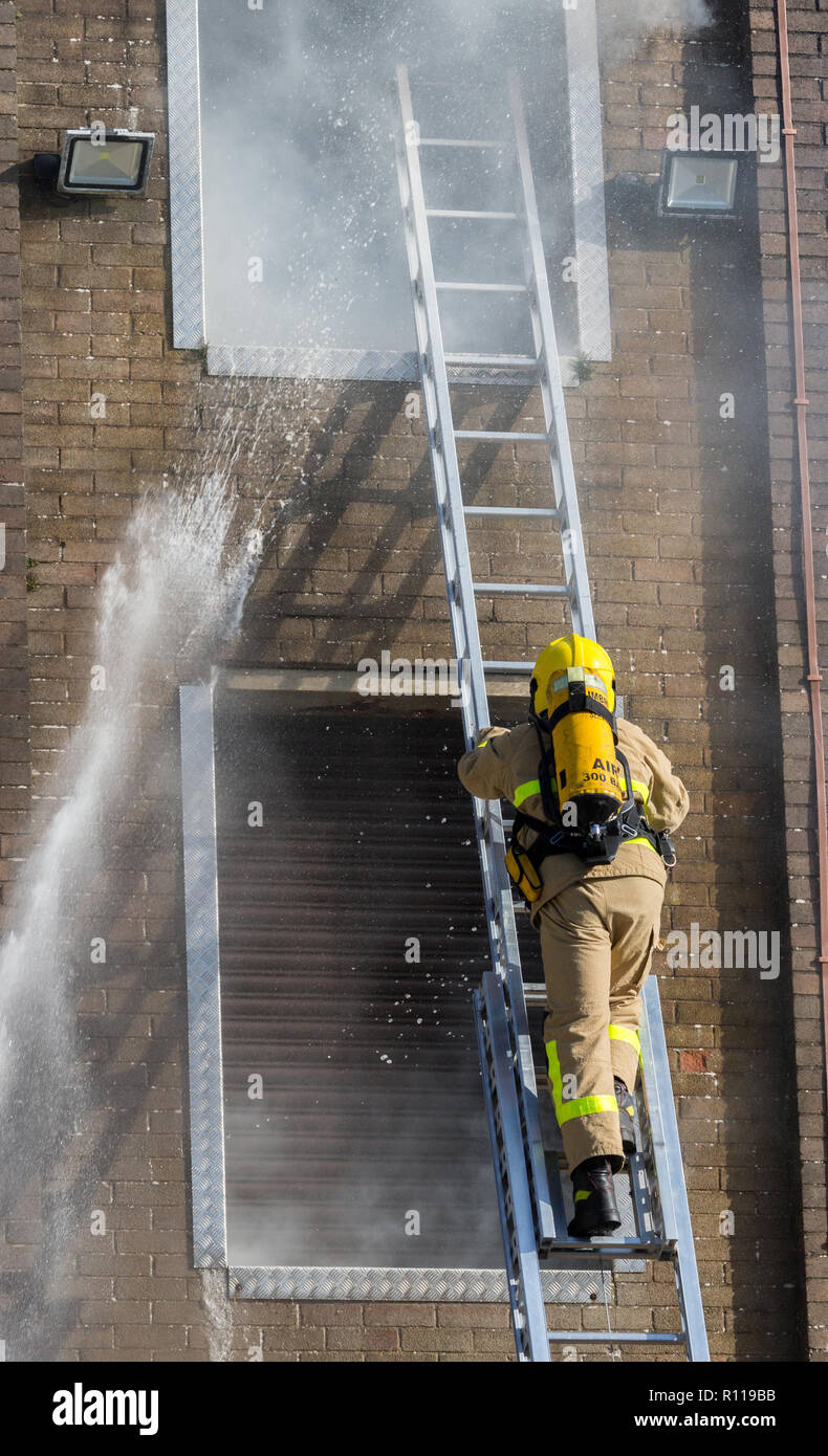 A firefighter using ladder access to enter a smoke filled tower during an exercise Stock Photo