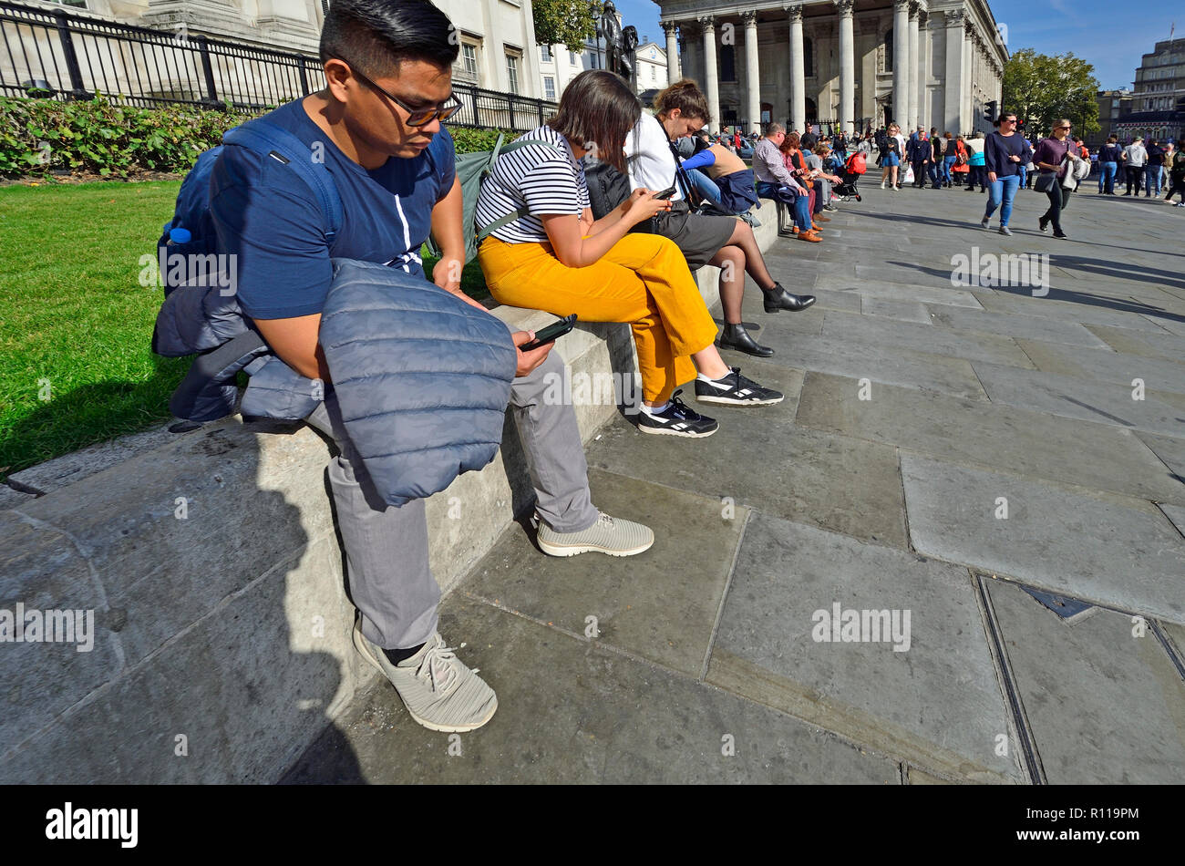 People on their mobile phones at lunchtime in front of the National Gallery in Trafalgar Square, London, England, UK. Stock Photo