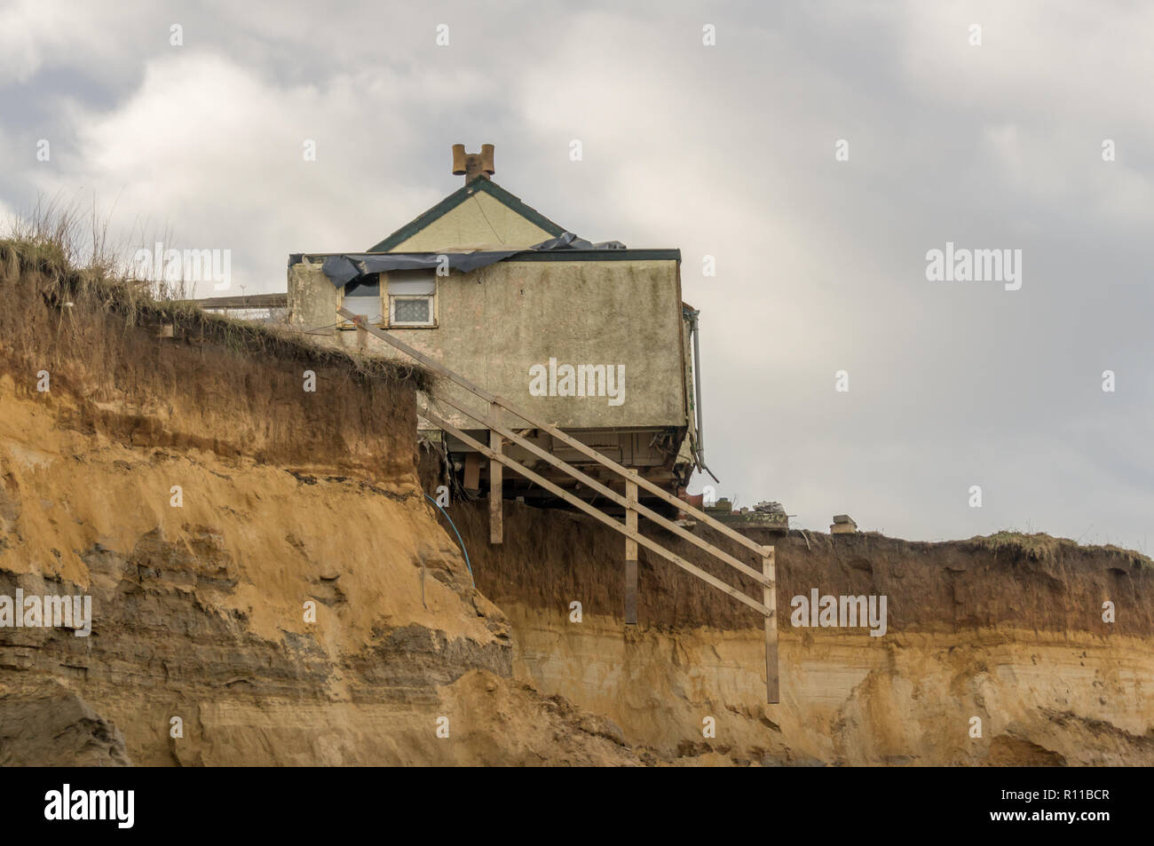 House on edge of cliff washed away by the sea, coastal erosion, global warming, rising sea levels, Happisburgh Norfolk, UK. side view Stock Photo