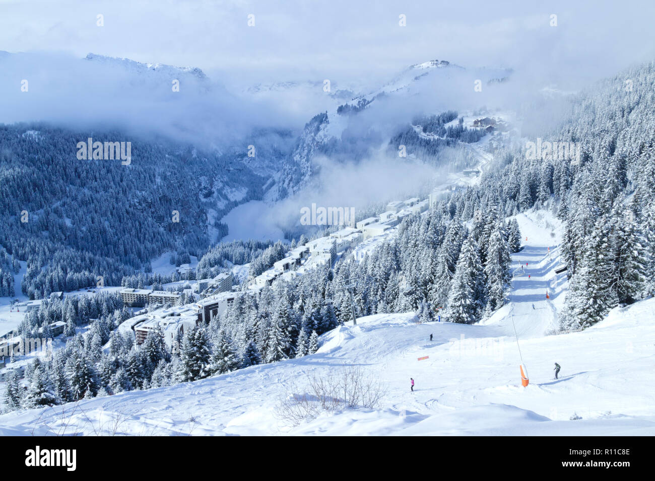Alpine landscape of ski and snowboard slopes through pine trees going down to winter resort of Flaine, Grand Massif, Alps, France , with low clouds in Stock Photo