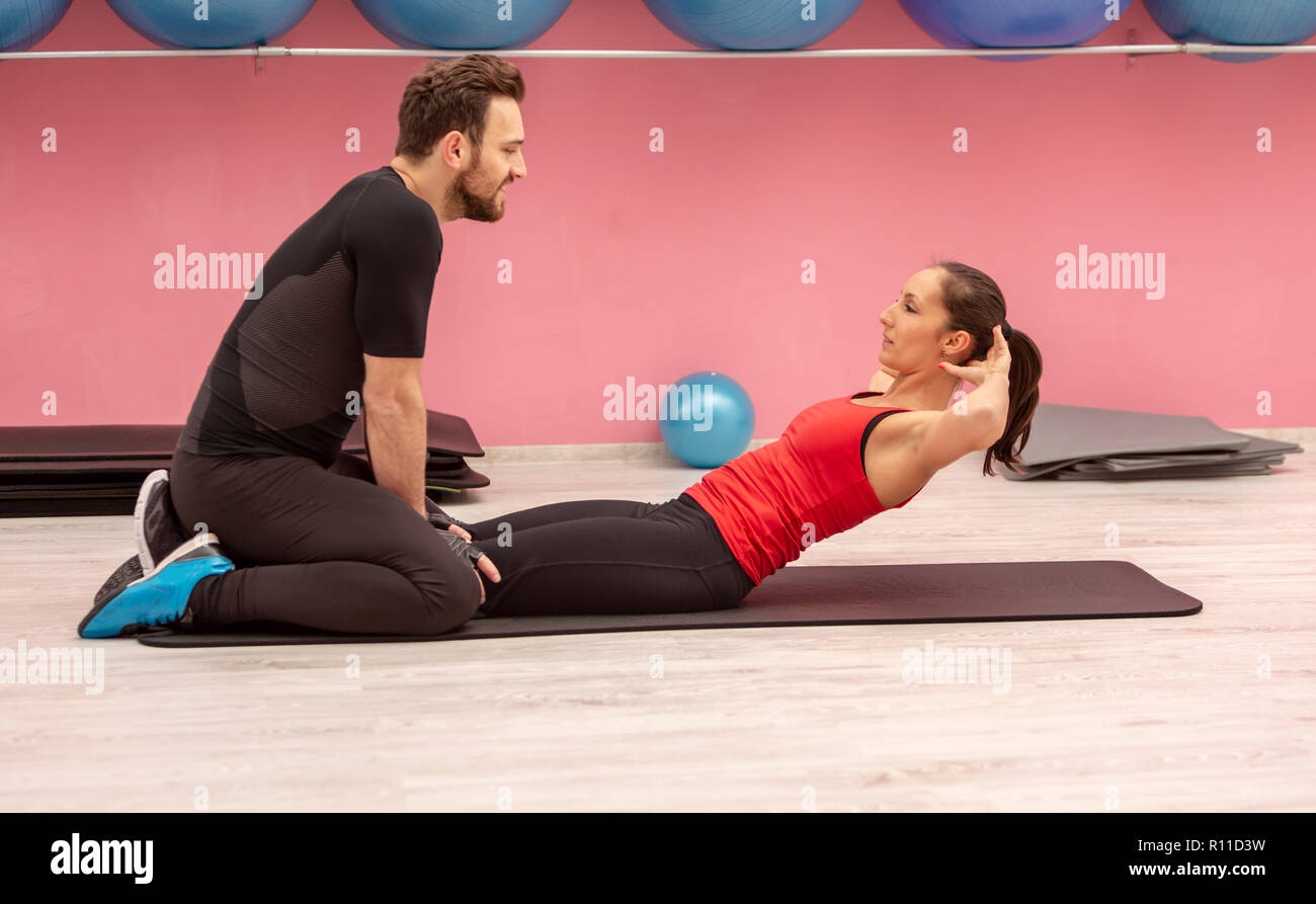 Young woman helped by his coach doing sit-ups in a gym Stock Photo - Alamy
