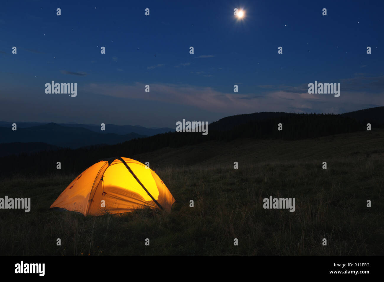 Illuminated orange tent at top of mountain at night Stock Photo