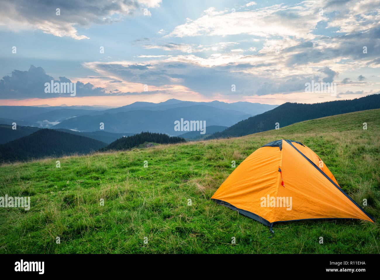Orange tent on green grass in mountains in summer Stock Photo
