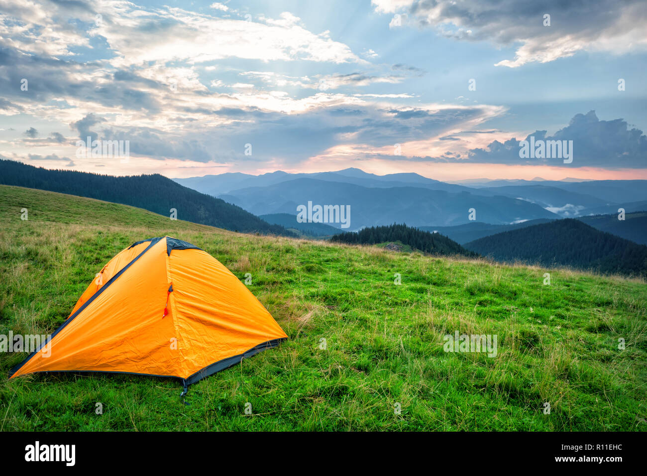 Orange tourist tent in mountains covered with green grass Stock Photo