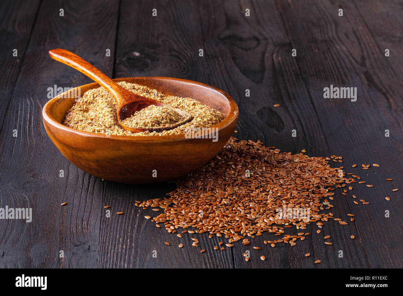 Brown flax seeds on spoon and flaxseed oil in glass jug on wooden table