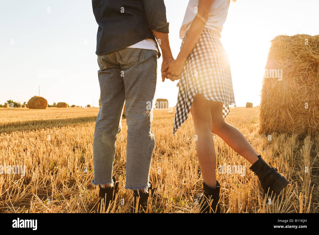 Cropped photo of guy and girl walking through golden field with bunch of haystacks during sunny day Stock Photo