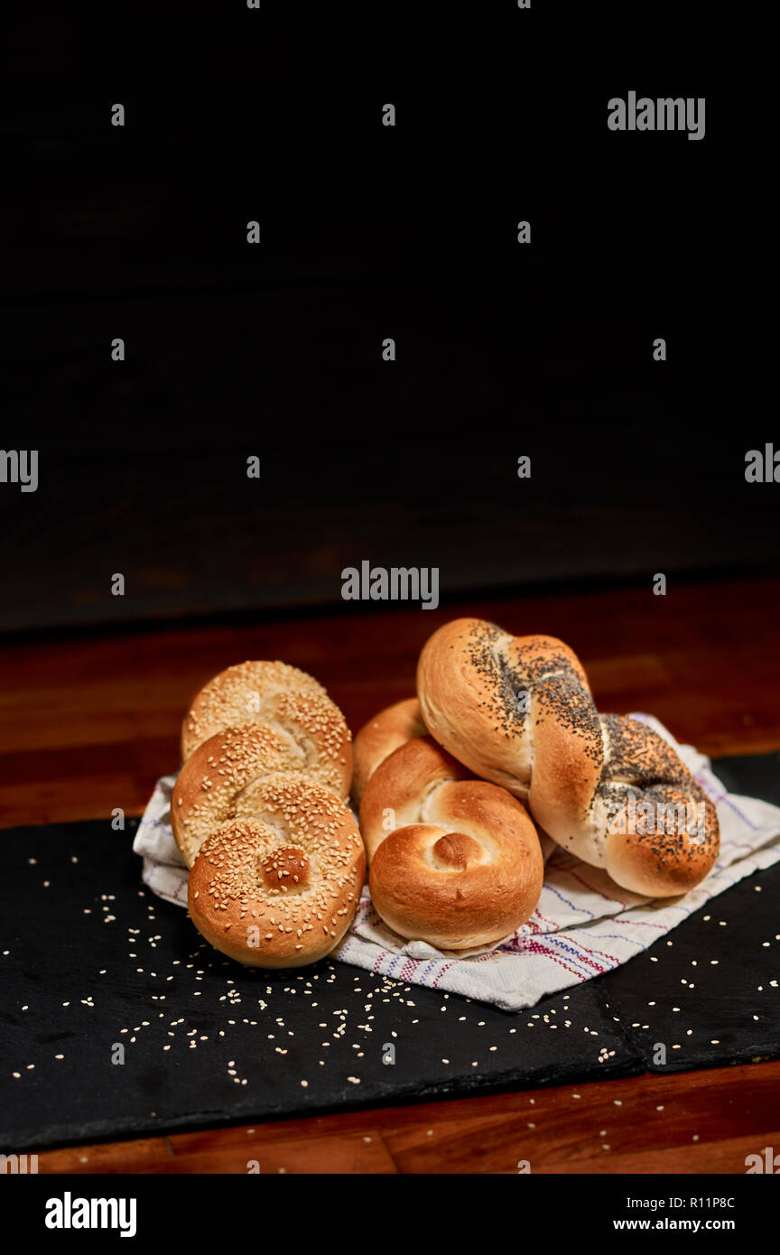 Freshly made poppy seed, seasame seed and plain bread braid on black stone cutting board, sprinkled with sesame seeds. Very shallow depth of field Stock Photo