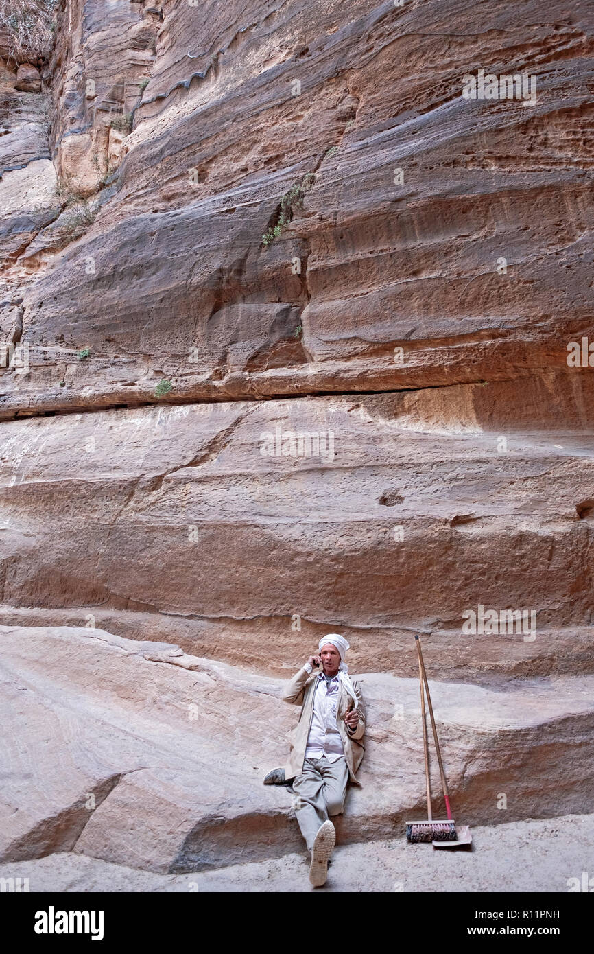 A Jordanian worker with a broom  and shovel resting & talking on his cell phone in Petra a historical and archeological city in South Jordan. Stock Photo