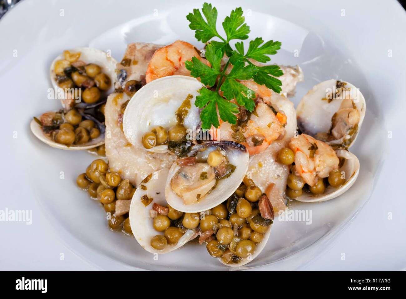 Hake in clam sauce and prawns with peas. Stock Photo