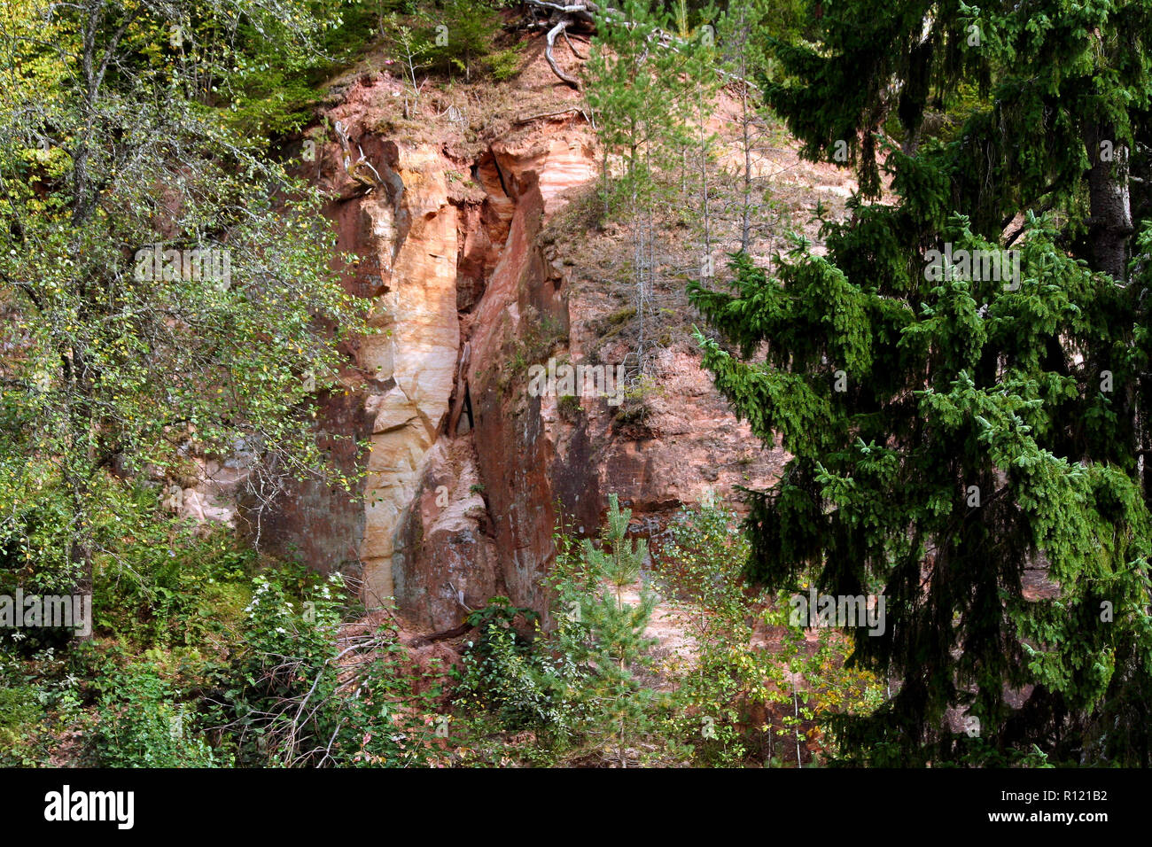 piece of rock red, yellow, brown, white shades, large cliff surrounded by green and yellowing vegetation in autumn, foreground on the left side Stock Photo