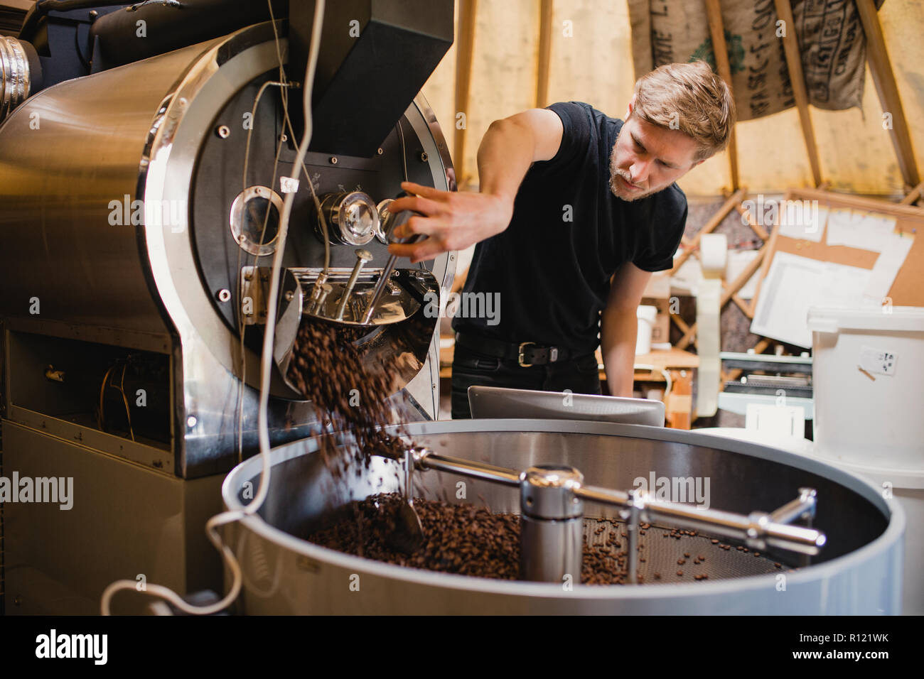 Male coffee shop employee using a coffee bean roasting machine and turning a dial to release the coffee beans. Stock Photo