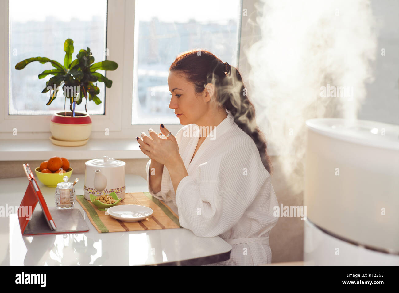 https://c8.alamy.com/comp/R1226E/woman-drinking-tea-reading-tablet-near-humidifier-R1226E.jpg