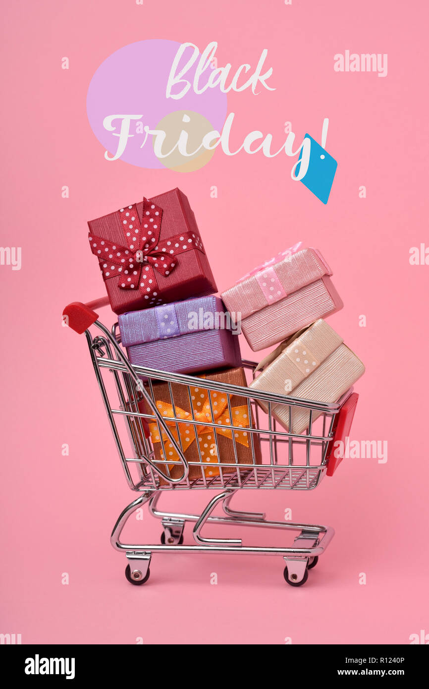 a shopping cart full of gifts of different colors and the text Black Friday on a pink background Stock Photo