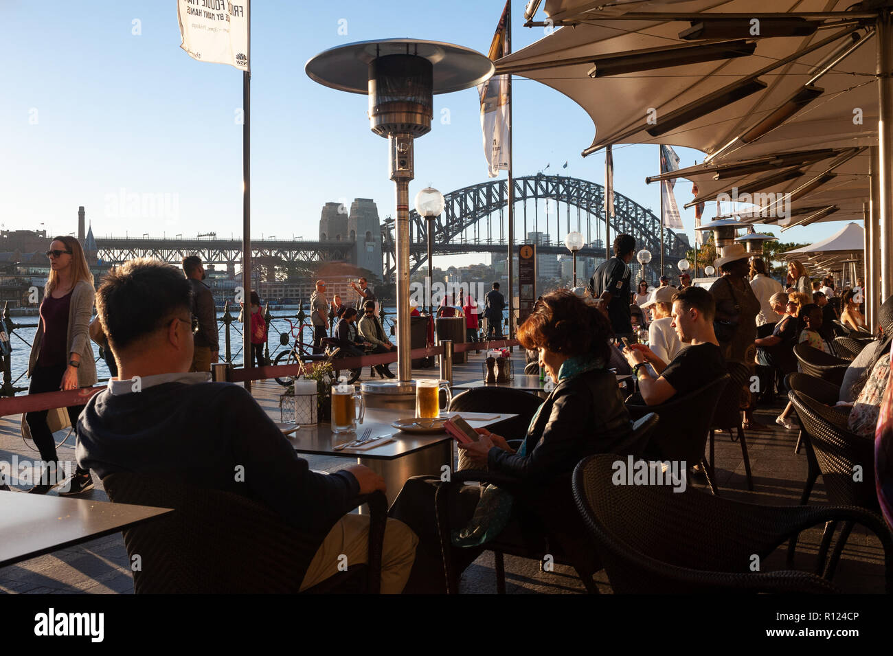 06.05.2018, Sydney, New South Wales, Australia - People are sitting in a restaurant along Circular Quay with the Sydney Harbour Bridge in the backdrop Stock Photo