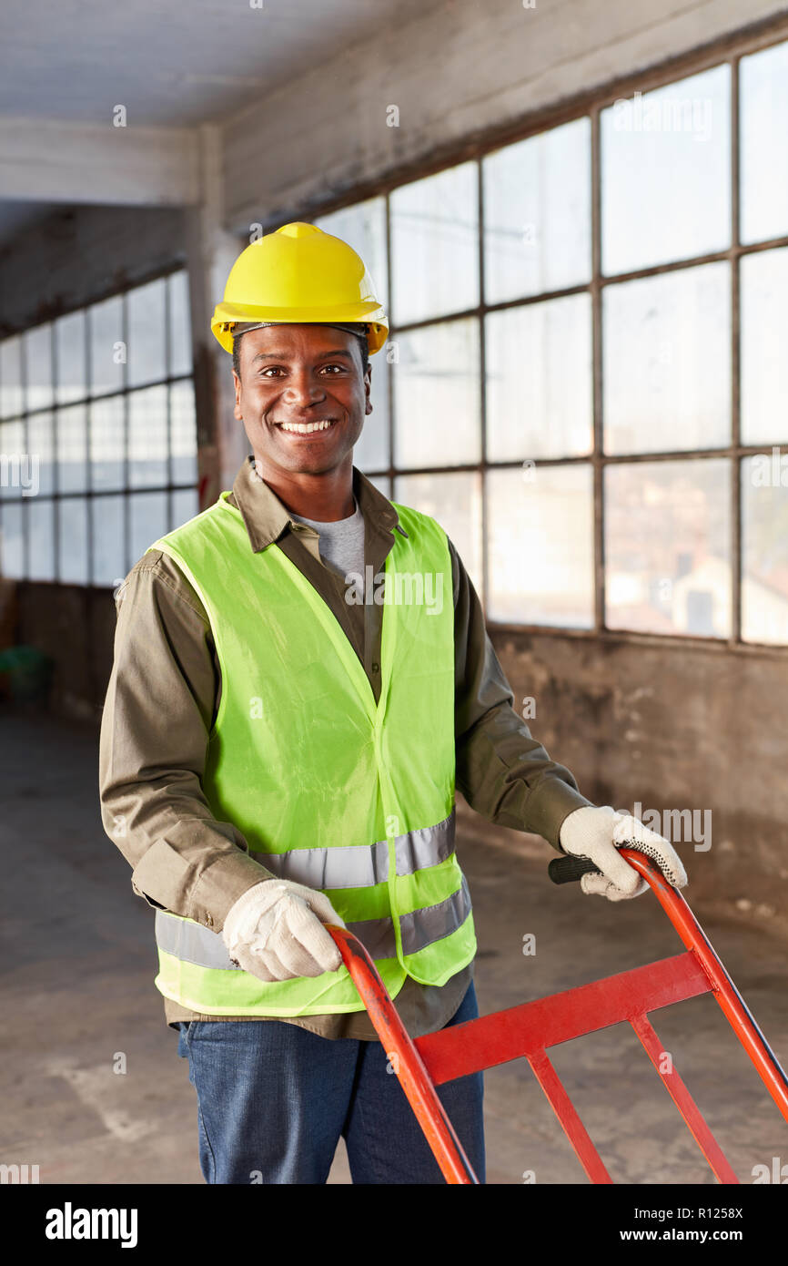 Logistics worker as apprentice of a freight forwarding with handcart in an empty hall Stock Photo