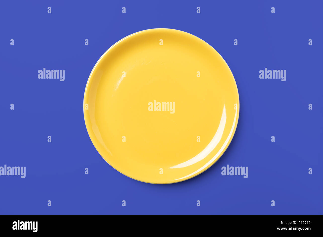 Yellow pastel plate on complementary blue background, pop art syle, view directly from above Stock Photo