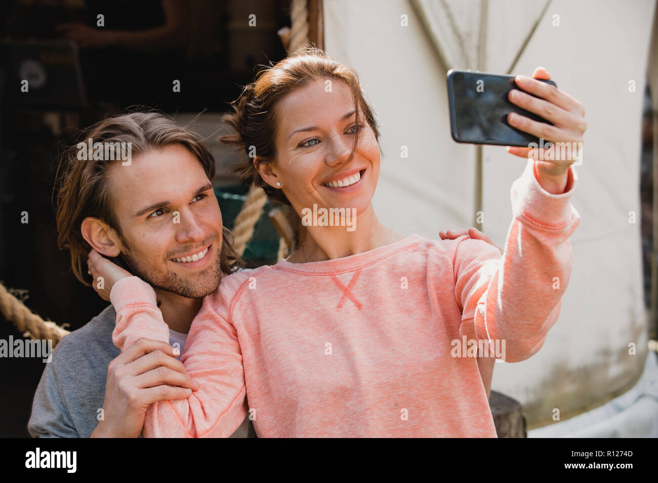 Mid-adult couple sitting outside looking and smiling at a smart phone as they take a selfie. Stock Photo