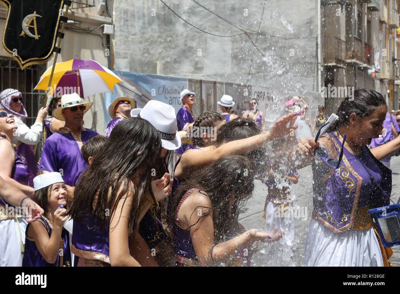 People under a water jet from Moros Almohabenos company on a street parade during the Moors and Christians historical reenactment in Orihuela, Spain Stock Photo