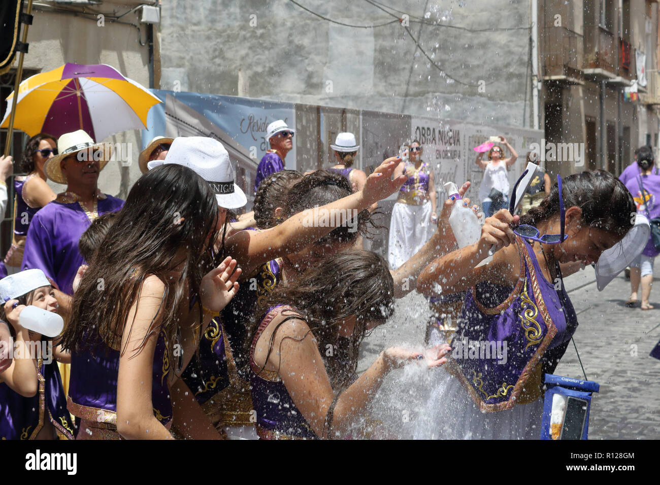 People under a water jet from Moros Almohabenos company on a street parade during the Moors and Christians historical reenactment in Orihuela, Spain Stock Photo