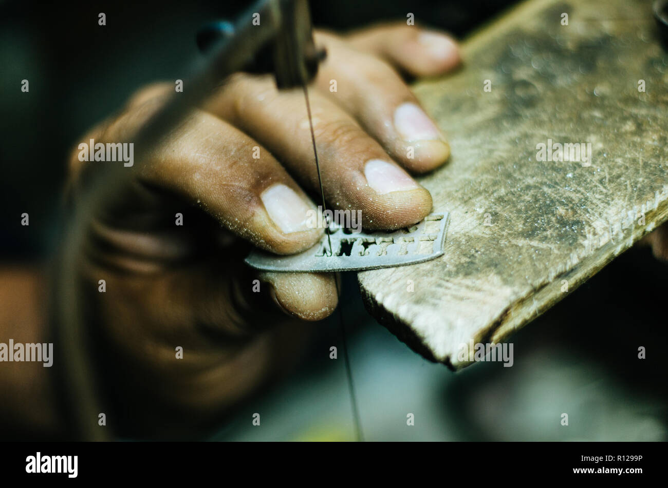 man's hands goldsmith work on a piece of silver with a metal saw on the work table, close up, selected focus, narrow depth of field Stock Photo