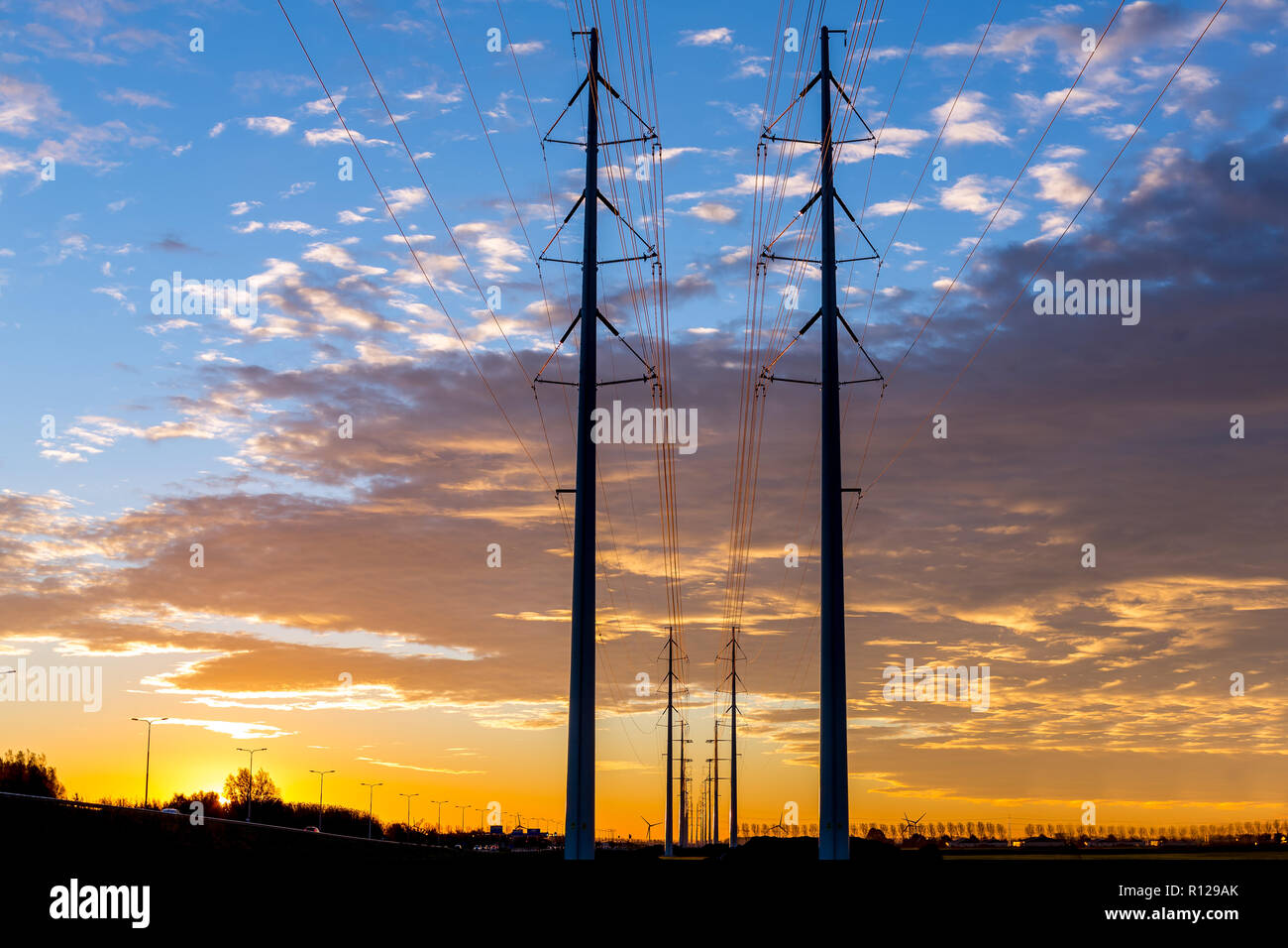 NIEUW-VENNEP, THE NETHERLANDS - November 07, 2018: Electric power lines at sunrise with perspective and horizon against a colorful cloudy sky. Stock Photo