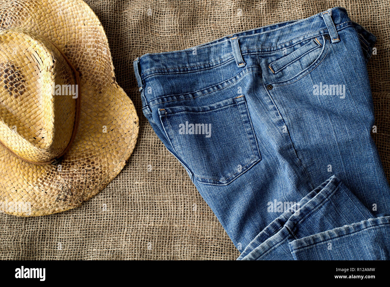 Blue jeans and country style straw hat on burlap. Top down view. Stock Photo