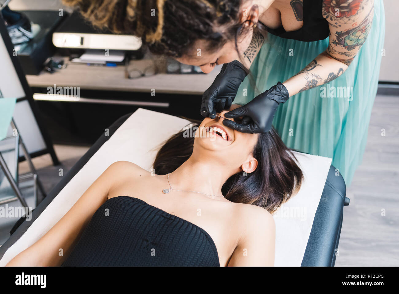 Tattooist piercing nose of customer in parlour Stock Photo