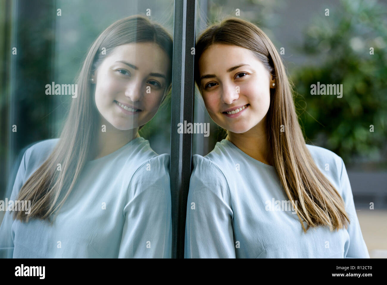 Woman and her mirror reflection on glass wall Stock Photo