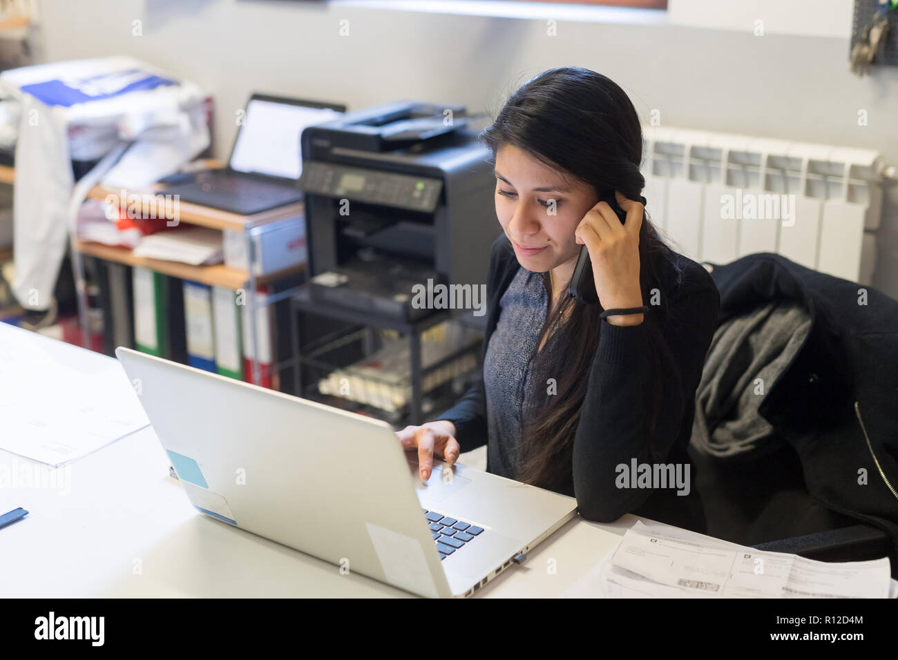 Woman using laptop and telephone in office Stock Photo