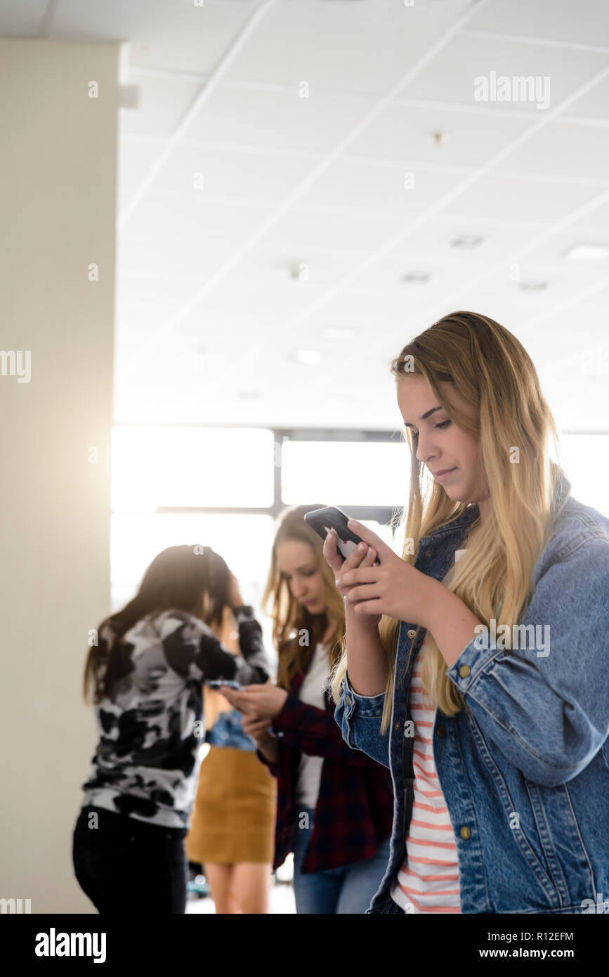 Female students looking at smartphones in university corridor Stock Photo