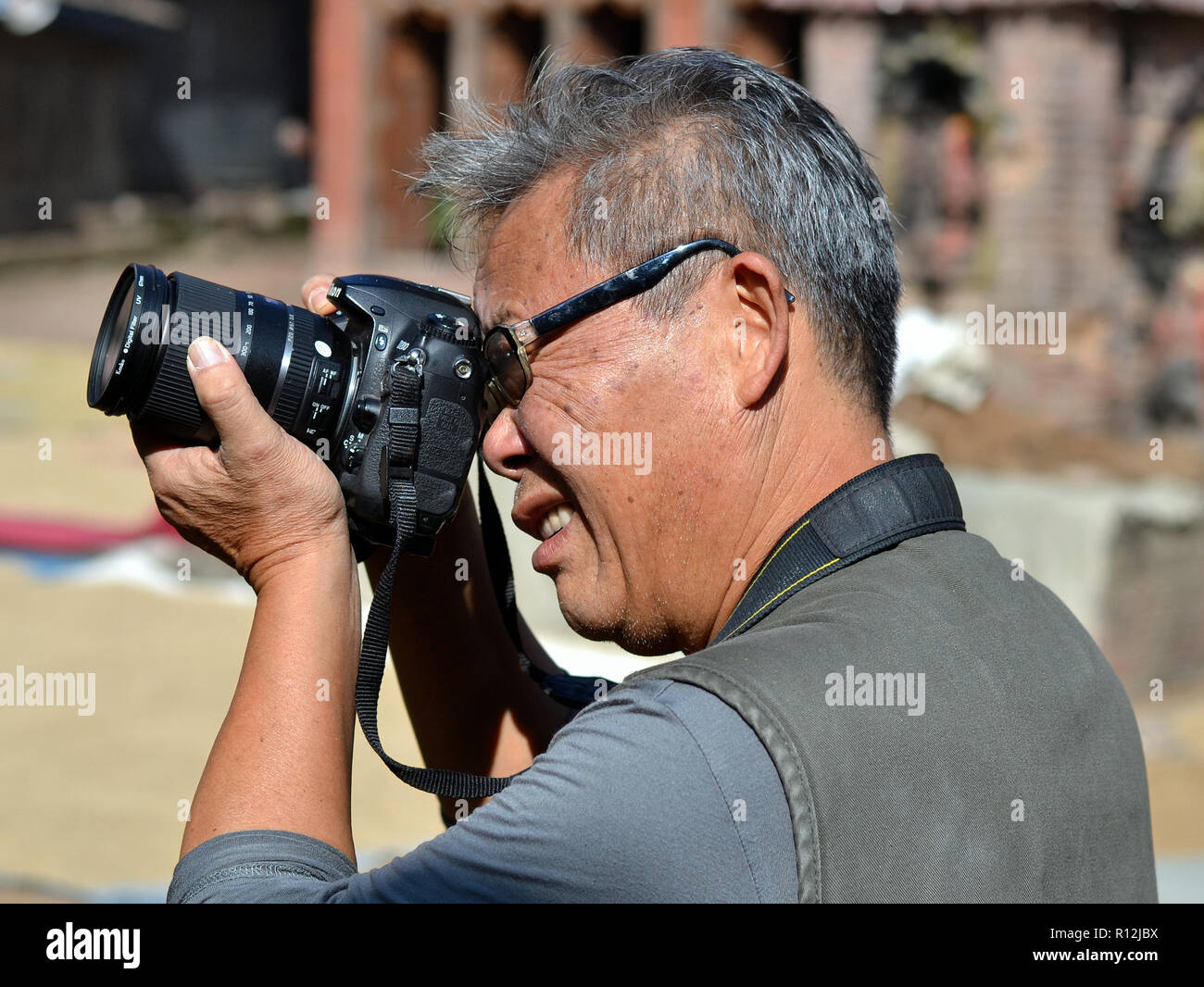 Middle-aged Chinese male street photographer takes aim with his Nikon DSLR camera. Stock Photo