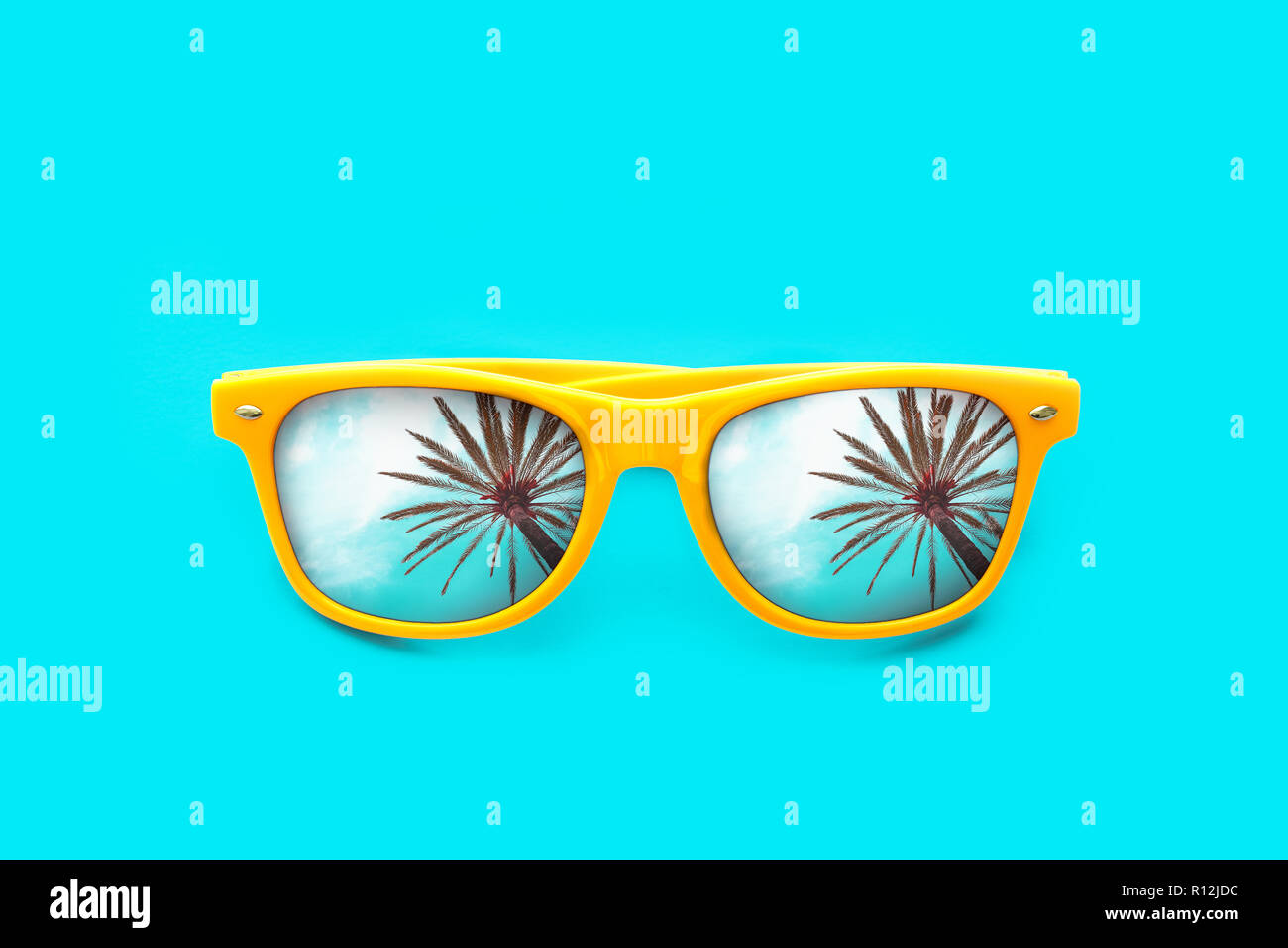 Yellow sunglasses with palm tree reflections isolated in intense cyan blue background. Minimal image concept for ready for summer, sun protection, hot Stock Photo