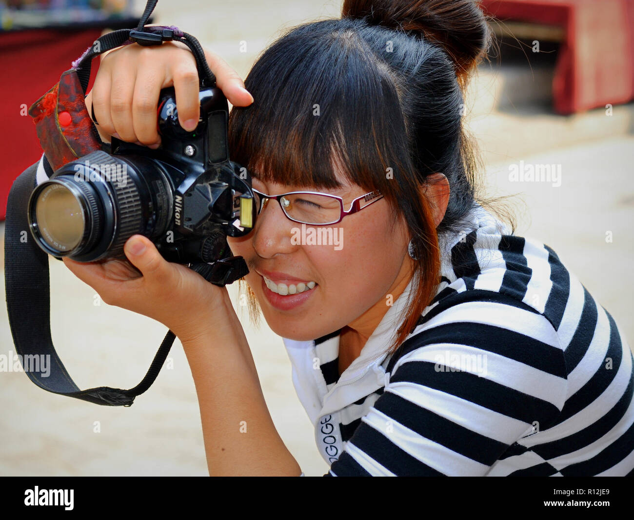 Young Chinese female street photographer takes a photo with her Nikon camera. Stock Photo