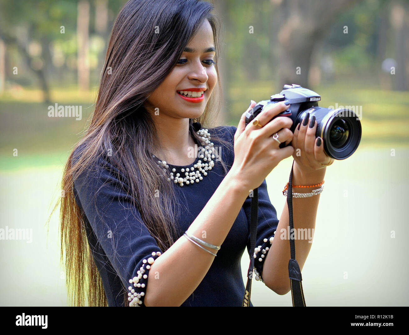Young Indian female photographer with very long hair looks at the camera screen of her Nikon D7200 DSLR camera. Stock Photo