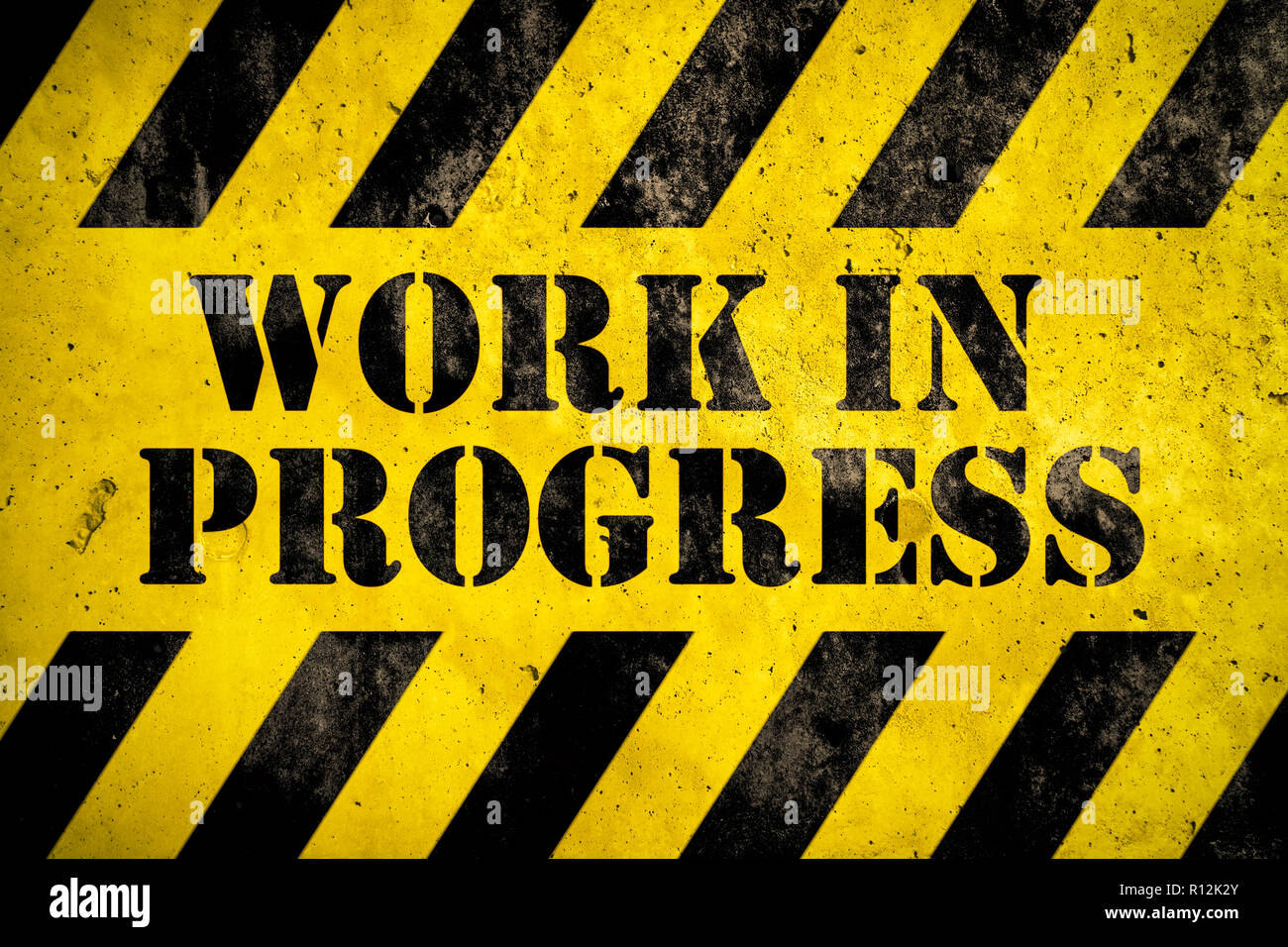 Work in progress warning sign stencil with yellow and black stripes painted over concrete wall cement texture background. Concept for do not enter the Stock Photo