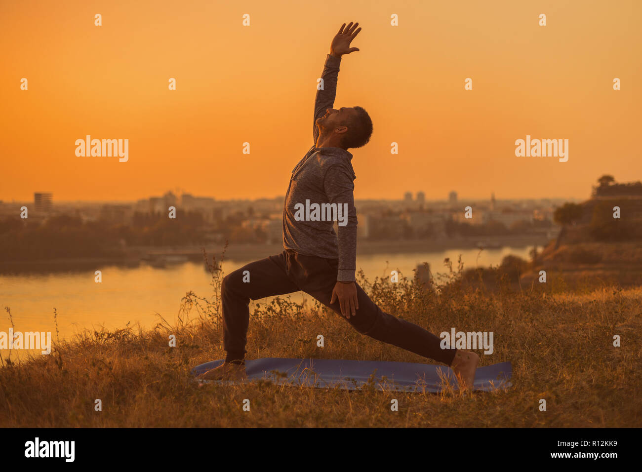 Man doing yoga on sunset with city view, Warrior 1 Pose/Virabhadrasana I Stock Photo