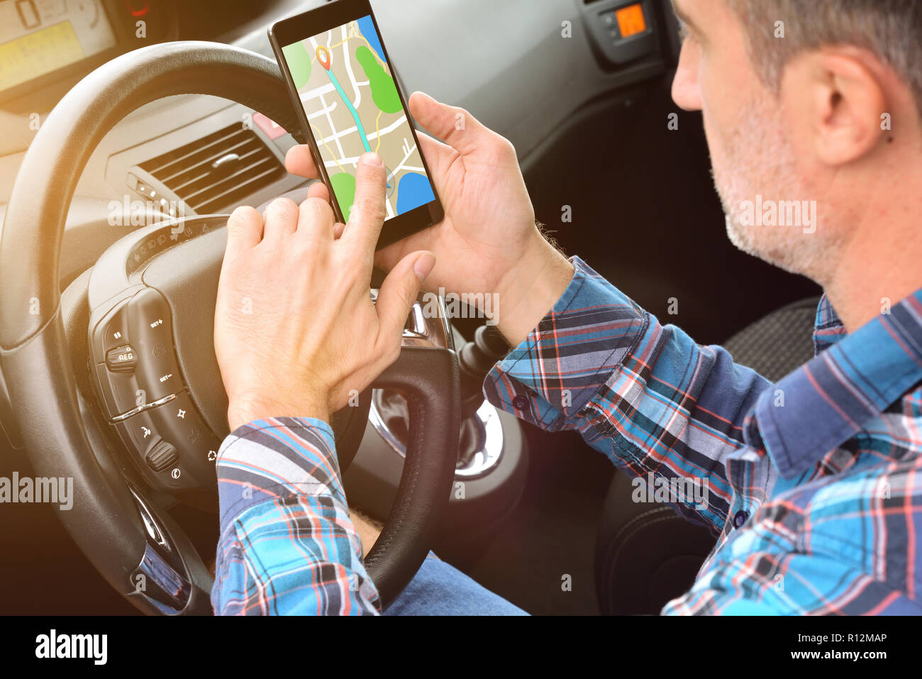 Man creating a route on a cell phone with an application to reach his destination in a car. Elevated rear view Stock Photo