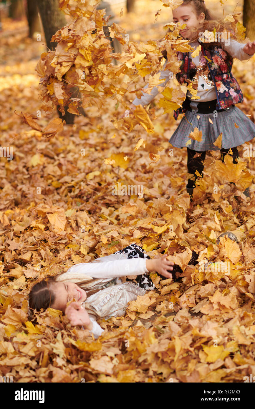 Child girl is lying and playing in fallen leaves in autumn city park ...