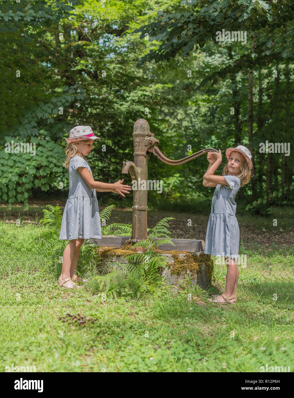 Two twin sisters near ancient water column in public park. Vintage