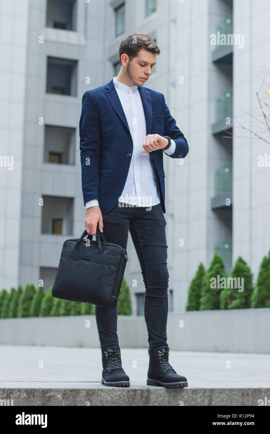 Young businessman in his hand the briefcase. The guy in the blue jacket looks at his watch. Stock Photo