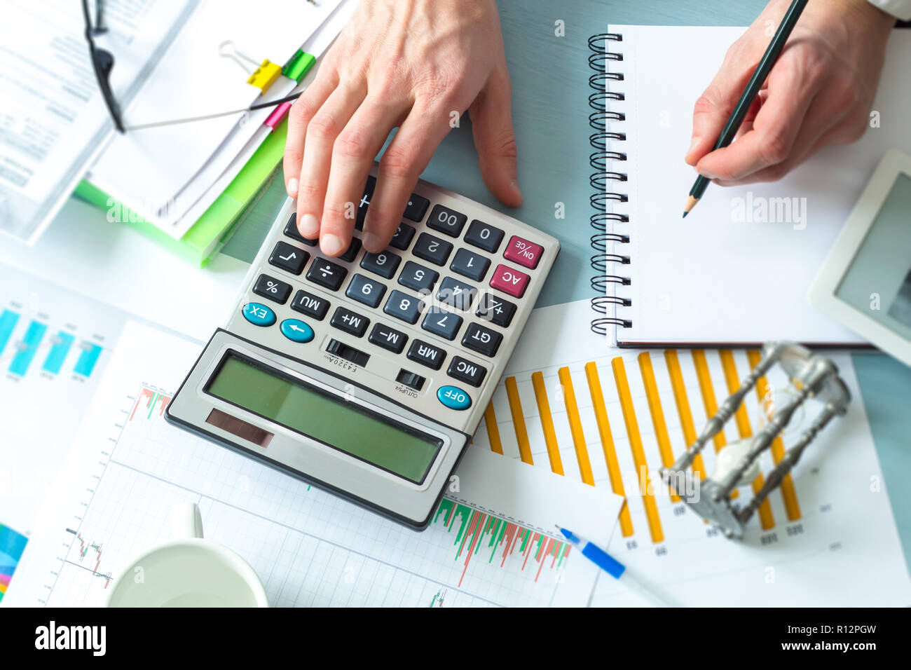 A business person, an accountant, compiles a financial report using a calculator while sitting at a desk in the office. Stock Photo