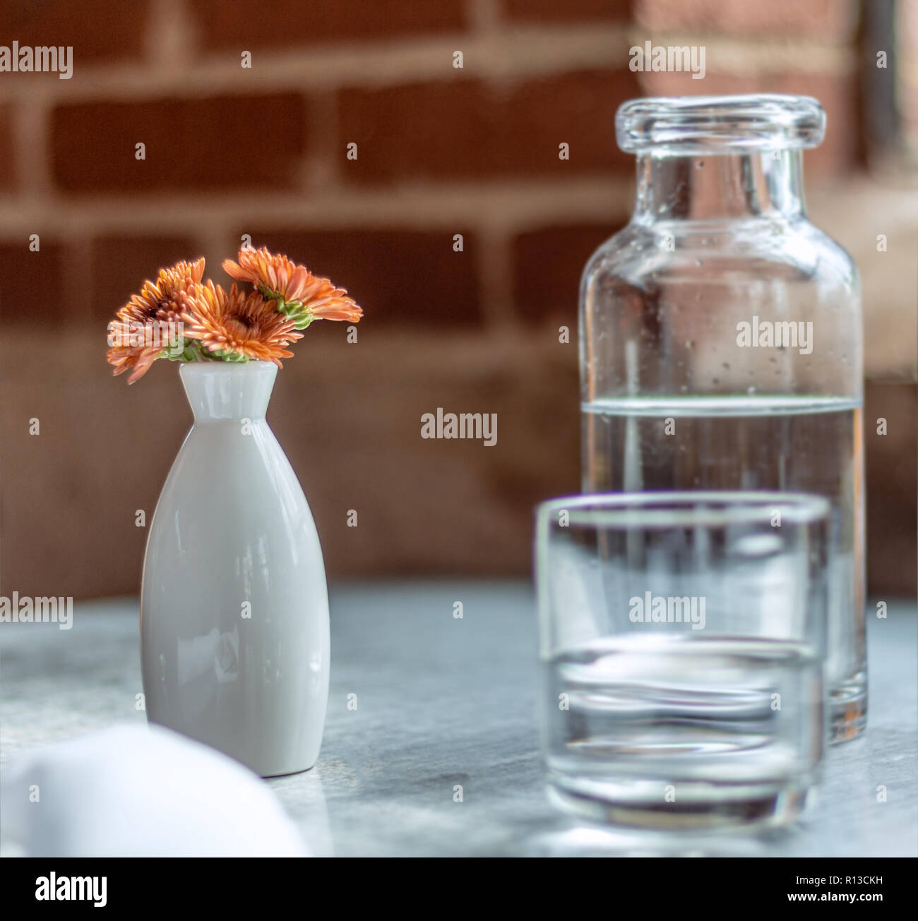 Casual Coffee shop. Latte art. Foaming latte. Water jug in clear glass. orange flowers in a white oval white vase. Stock Photo