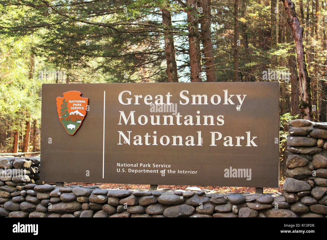 Daytime photo of a Great Smoky Mountains National Park entrance sign with stone surrounding and trees and sunshine in the background Stock Photo