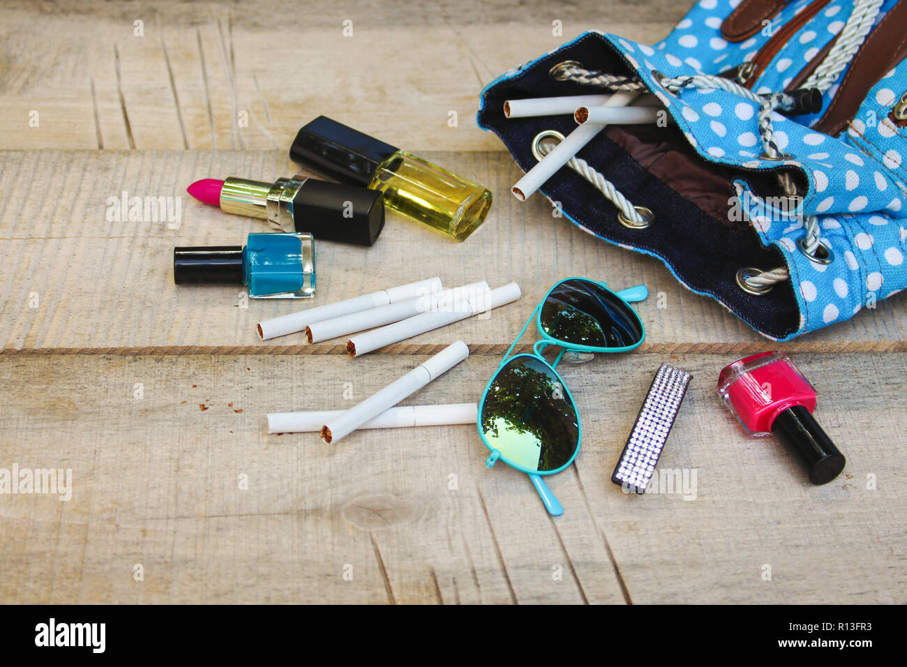 Cosmetics and cigarettes fell out of the backpack of a teenager on a wooden  background Stock Photo