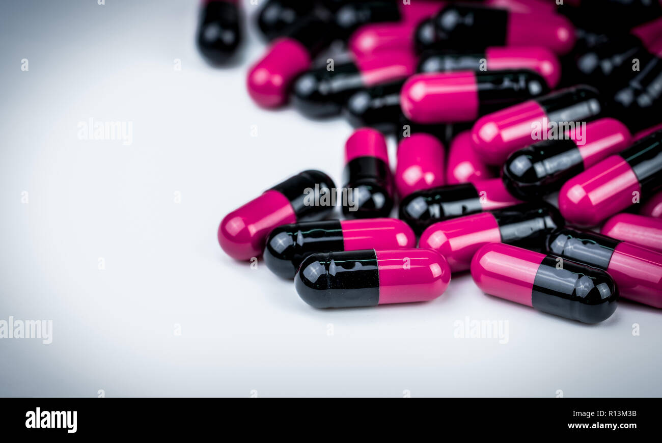 Pink-black capsule pills on white table. Antibiotics drug resistance. Global healthcare. Antimicrobial capsule pills. Pharmacy background. Antibiotic  Stock Photo