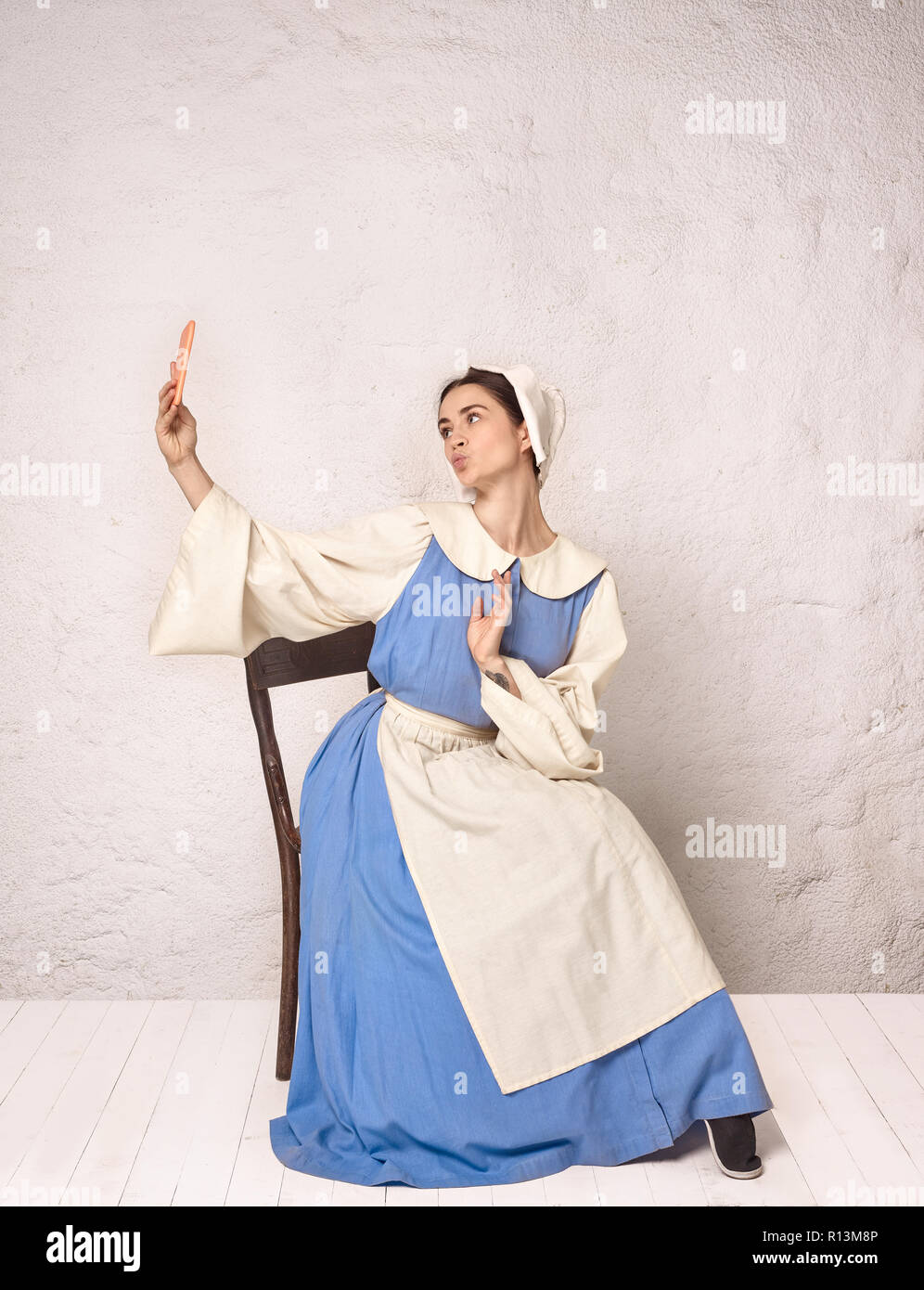 Medieval Woman in Historical Costume Wearing Corset Dress and Bonnet. Beautiful peasant girl wearing thrush costume with mobile phone Stock Photo