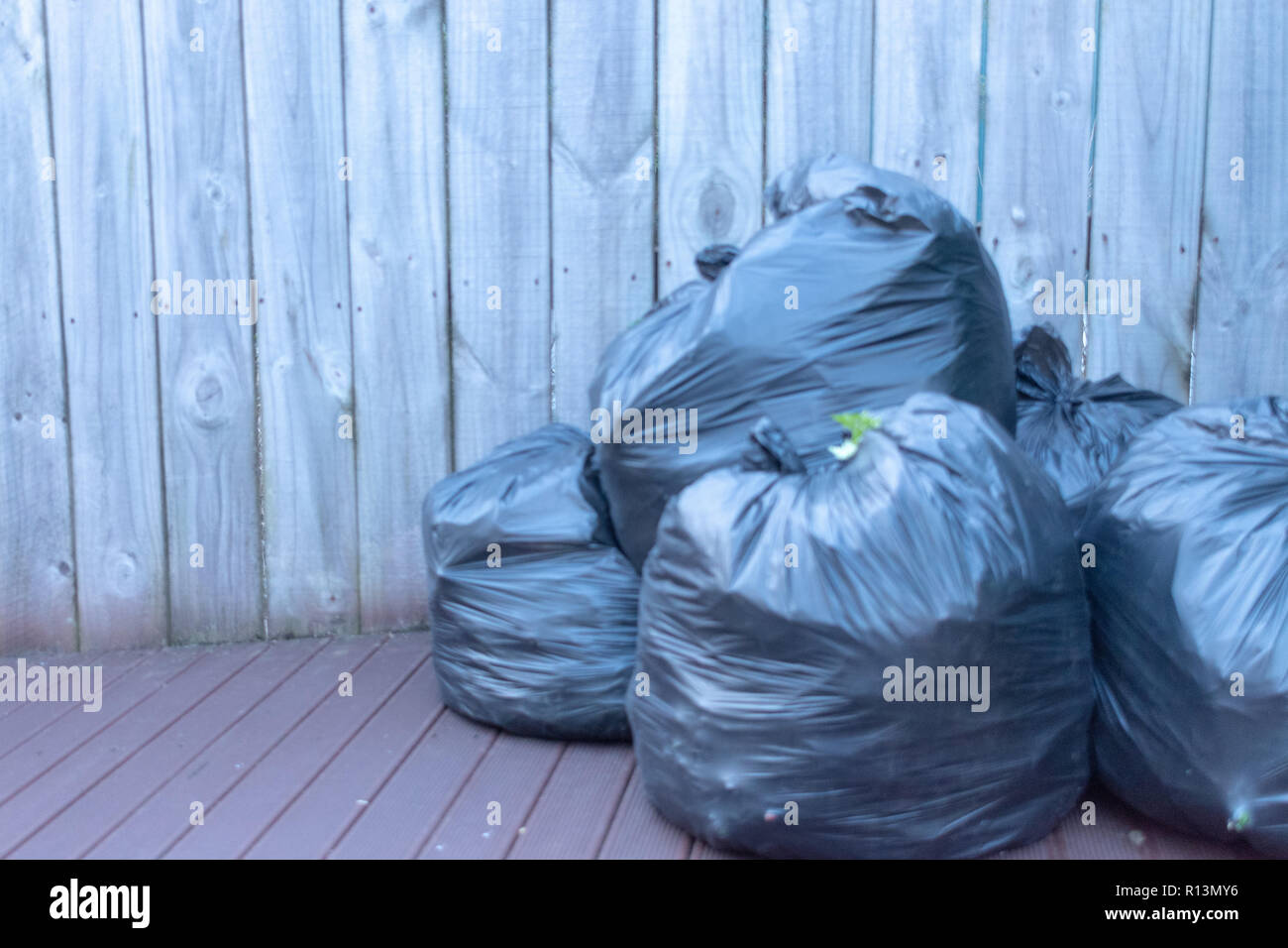 https://c8.alamy.com/comp/R13MY6/horizontal-image-of-three-black-plastic-garbage-bags-packed-and-ready-to-take-out-sitting-on-the-deck-against-a-wooden-fence-R13MY6.jpg