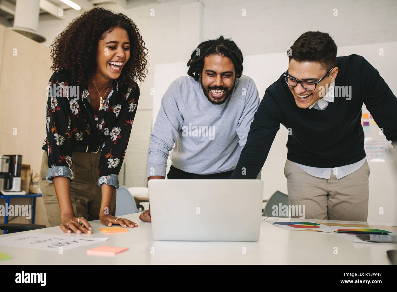 businessmen and woman having fun during work and laughing. business colleagues standing together in office looking at a laptop computer and laughing. Stock Photo