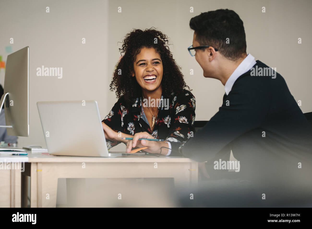 Happy business colleagues discussing ideas sitting at the desk with laptop computer. Businessman and woman working as a team in office. Stock Photo