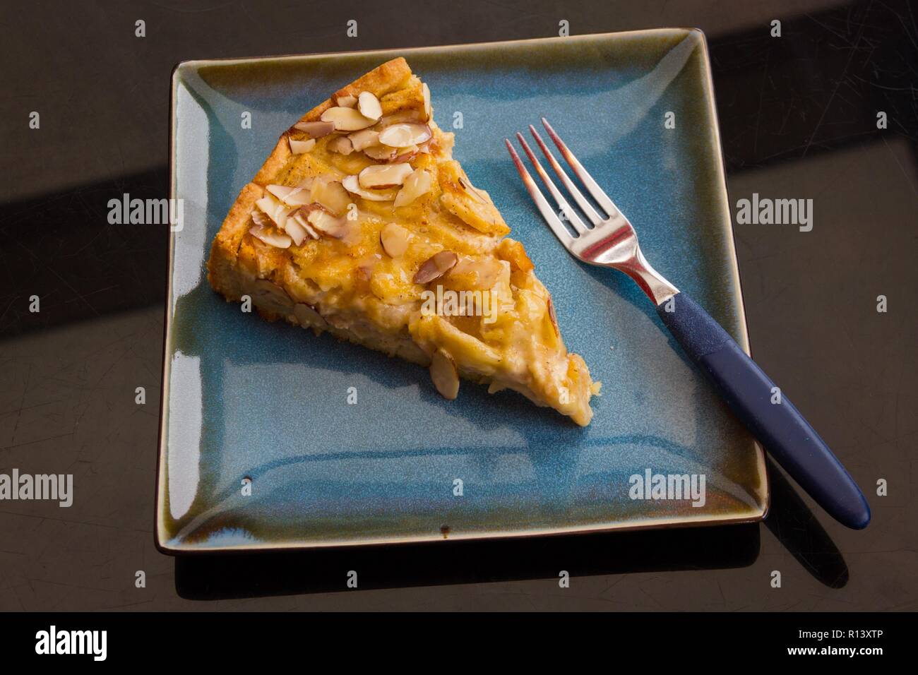 Top view of tasty apple almond kuchen cake and fork on blue square plate. Restaurant delicatessen dessert concept Stock Photo